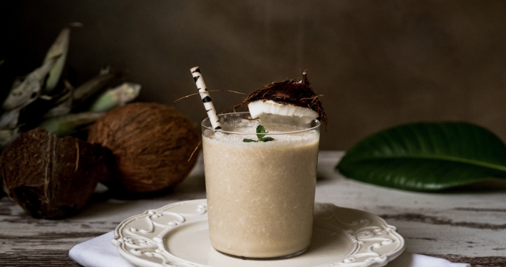 Glass of homemade coconut milk on a plate with a birch straw and coconuts in the background